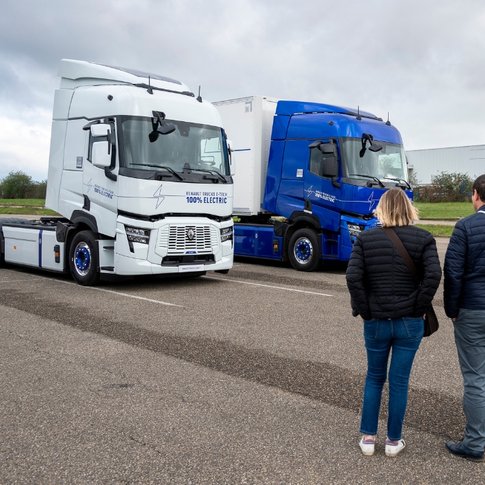 Two Renault Trucks electric trucks, one white and one blue, observed by two people outdoors